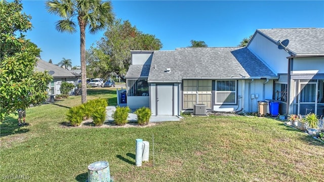 back of property with a yard, a sunroom, and a shingled roof