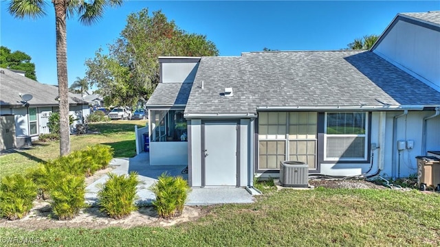 back of property with a yard, central AC unit, a sunroom, and roof with shingles