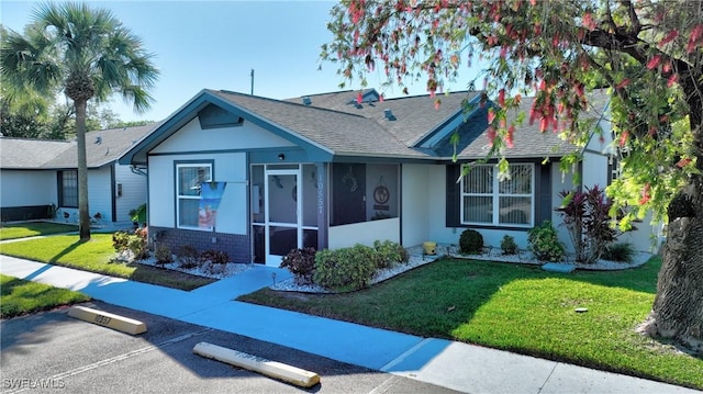 view of front of home with stucco siding, a front lawn, uncovered parking, roof with shingles, and a sunroom