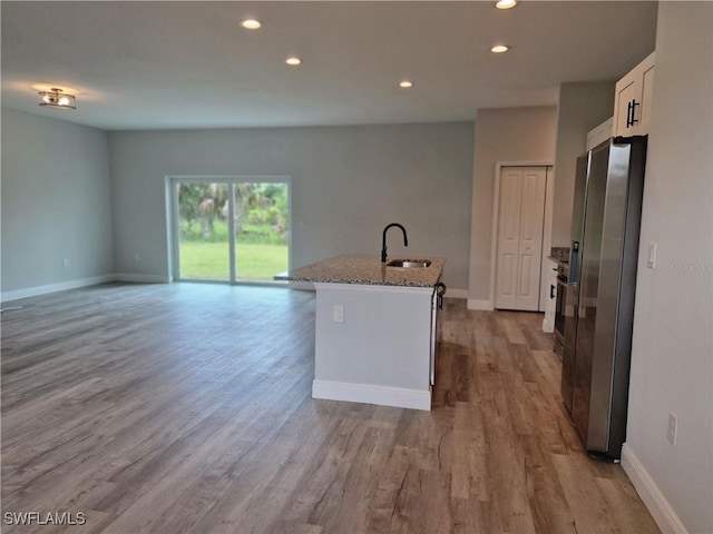 kitchen with light stone counters, recessed lighting, a sink, stainless steel refrigerator with ice dispenser, and a center island with sink