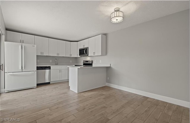 kitchen featuring baseboards, light wood-style flooring, stainless steel appliances, light countertops, and white cabinetry