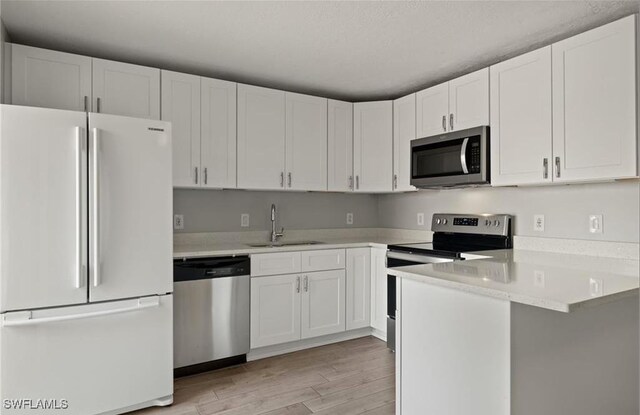 kitchen with a peninsula, a sink, light countertops, white cabinets, and appliances with stainless steel finishes