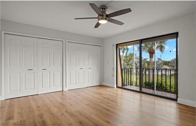 unfurnished bedroom featuring two closets, access to exterior, wood finished floors, baseboards, and ceiling fan