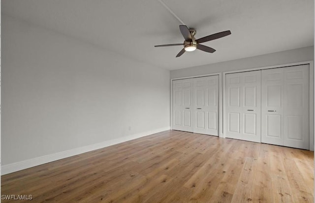 unfurnished bedroom featuring baseboards, a ceiling fan, multiple closets, and wood finished floors