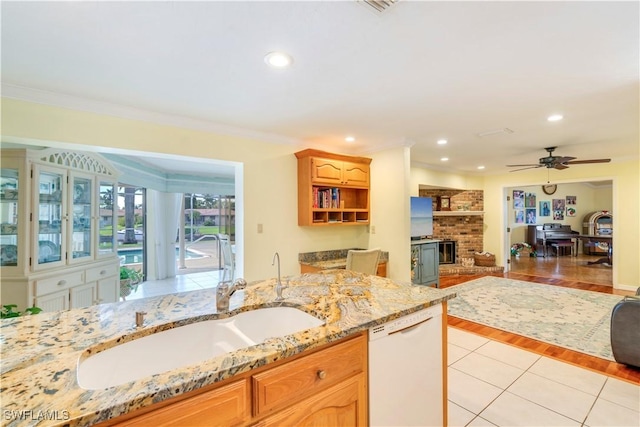 kitchen with light tile patterned floors, ornamental molding, a sink, light stone countertops, and dishwasher