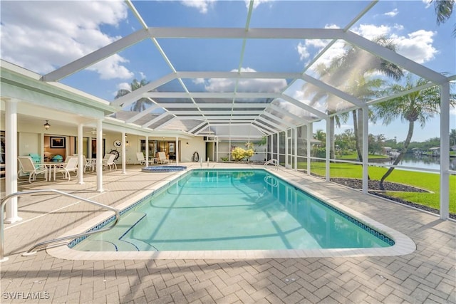 outdoor pool with glass enclosure, a patio area, a water view, and an in ground hot tub