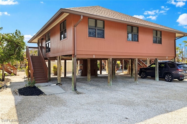 coastal inspired home with a carport, a shingled roof, stairs, and gravel driveway