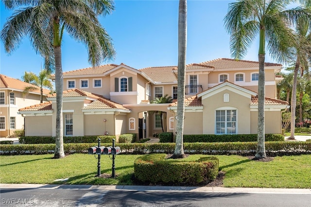 mediterranean / spanish-style house featuring a balcony, a tiled roof, a front yard, and stucco siding