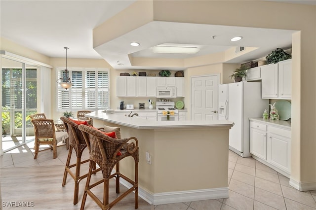 kitchen featuring white appliances, a kitchen bar, white cabinetry, and light countertops