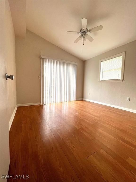 empty room with ceiling fan, baseboards, wood finished floors, and vaulted ceiling