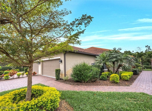 view of property exterior featuring decorative driveway, an attached garage, a tile roof, and stucco siding