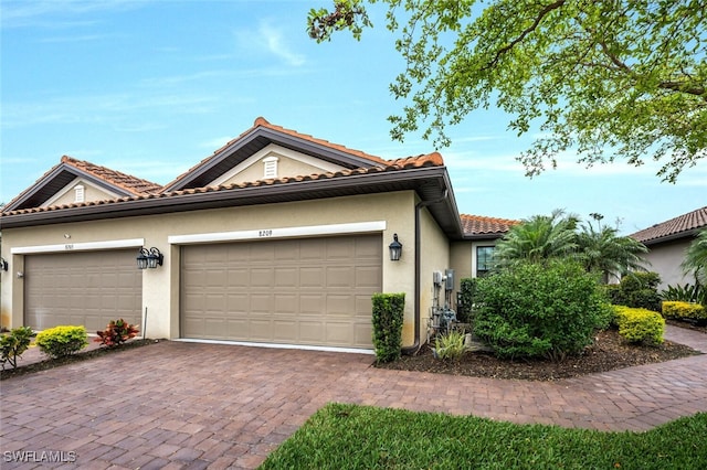 view of front of home with a garage, decorative driveway, a tiled roof, and stucco siding