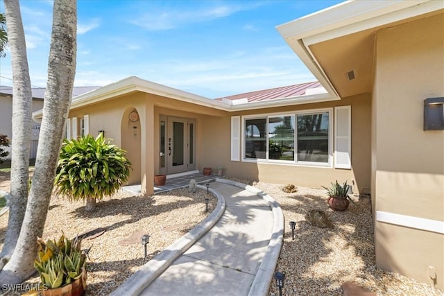 doorway to property featuring visible vents, stucco siding, french doors, metal roof, and a standing seam roof