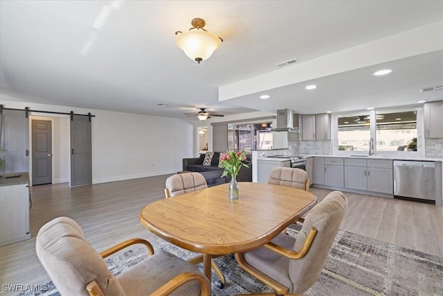 dining space featuring a barn door, visible vents, light wood-style floors, and a ceiling fan