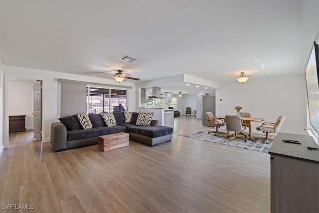 living room featuring a ceiling fan, visible vents, and light wood-type flooring