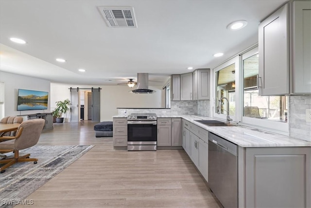 kitchen with visible vents, gray cabinetry, island range hood, stainless steel appliances, and a sink