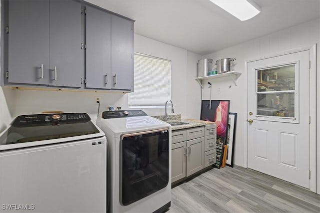 washroom featuring a sink, cabinet space, light wood-style floors, and independent washer and dryer