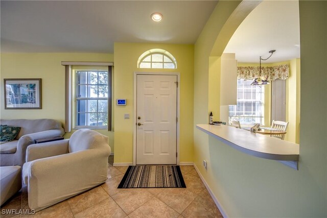 foyer featuring plenty of natural light, baseboards, arched walkways, and light tile patterned flooring