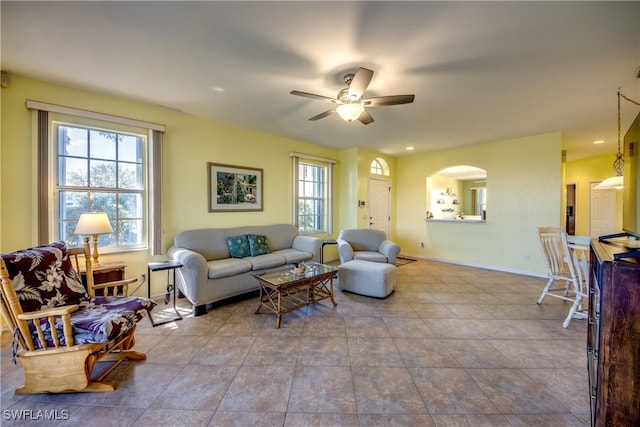 living area featuring ceiling fan, arched walkways, a wealth of natural light, and baseboards