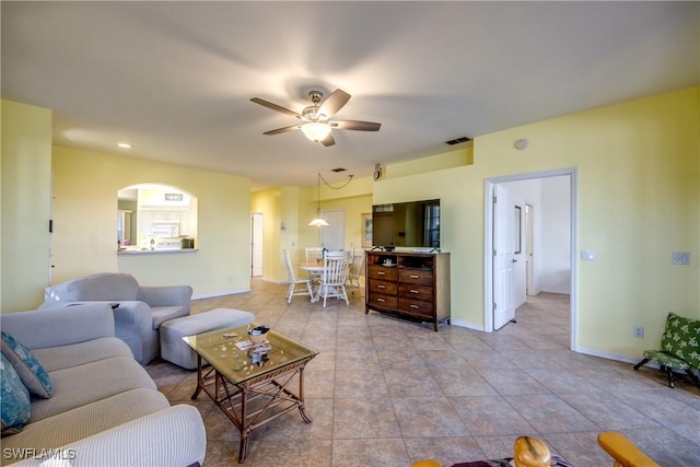 living area featuring light tile patterned floors, visible vents, arched walkways, baseboards, and ceiling fan