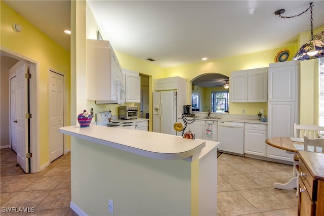 kitchen featuring arched walkways, a peninsula, white appliances, a sink, and light countertops