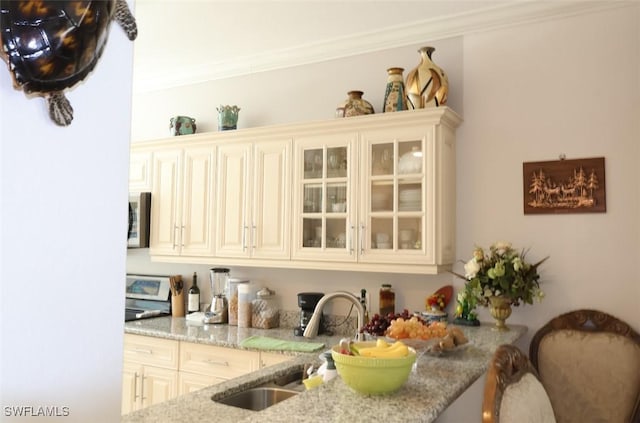 kitchen with glass insert cabinets, stainless steel microwave, ornamental molding, light stone countertops, and a sink