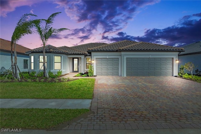 mediterranean / spanish house with a garage, a tiled roof, decorative driveway, stucco siding, and a front yard