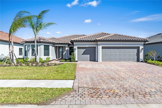 mediterranean / spanish home with a tiled roof, an attached garage, decorative driveway, a front yard, and stucco siding