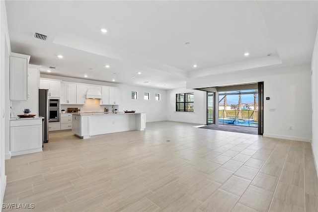 unfurnished living room featuring a raised ceiling, visible vents, and recessed lighting