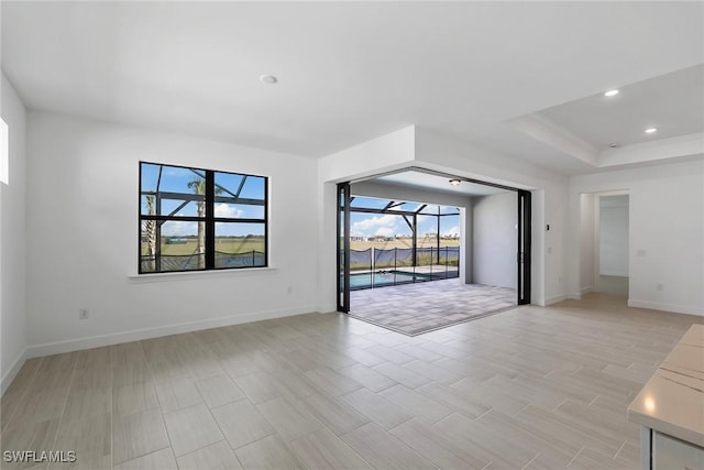 unfurnished room featuring baseboards, a sunroom, a tray ceiling, light wood-type flooring, and recessed lighting