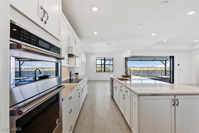 kitchen featuring light stone counters, stainless steel appliances, decorative backsplash, white cabinets, and a sink