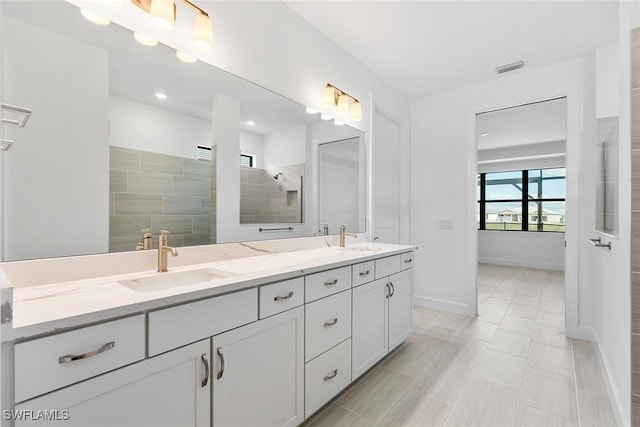 bathroom with tiled shower, a sink, baseboards, and double vanity