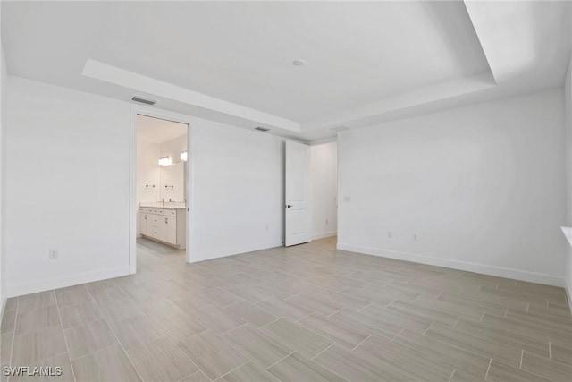 unfurnished bedroom with a tray ceiling, visible vents, and baseboards