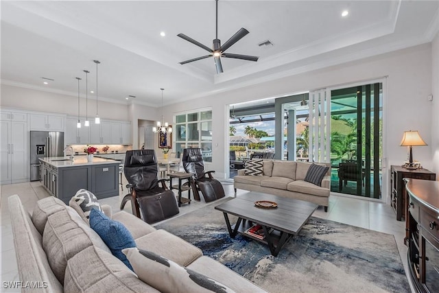 living room featuring light tile patterned floors, ceiling fan with notable chandelier, crown molding, and a tray ceiling