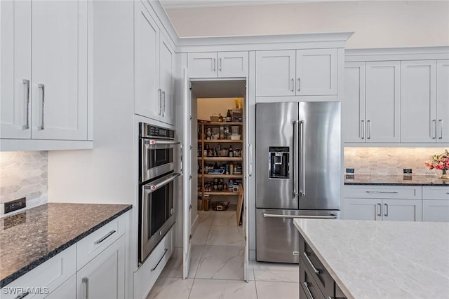 kitchen with marble finish floor, dark stone countertops, tasteful backsplash, appliances with stainless steel finishes, and white cabinets