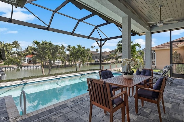 pool with glass enclosure, ceiling fan, a patio, and a water view