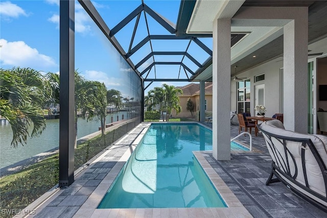 outdoor pool with glass enclosure, a water view, and a patio area