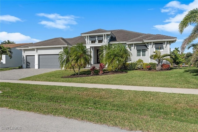 view of front of property featuring a tile roof, a front yard, stucco siding, decorative driveway, and an attached garage