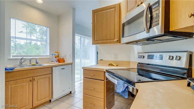 kitchen with light brown cabinetry, light countertops, light tile patterned flooring, stainless steel appliances, and a sink