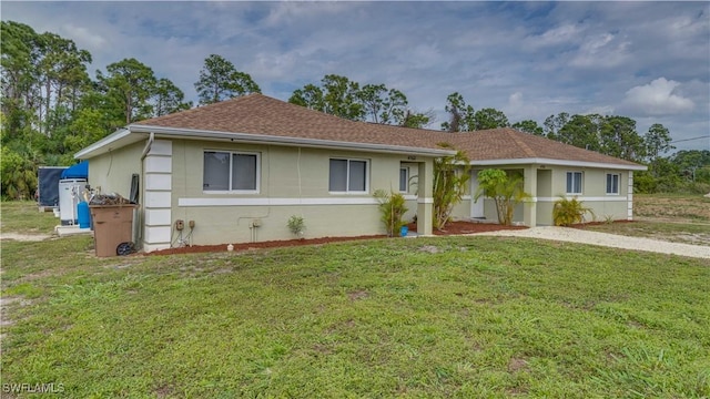 single story home with a front lawn, roof with shingles, and stucco siding