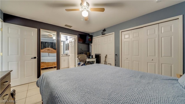 bedroom with visible vents, multiple closets, ensuite bath, light tile patterned floors, and ceiling fan