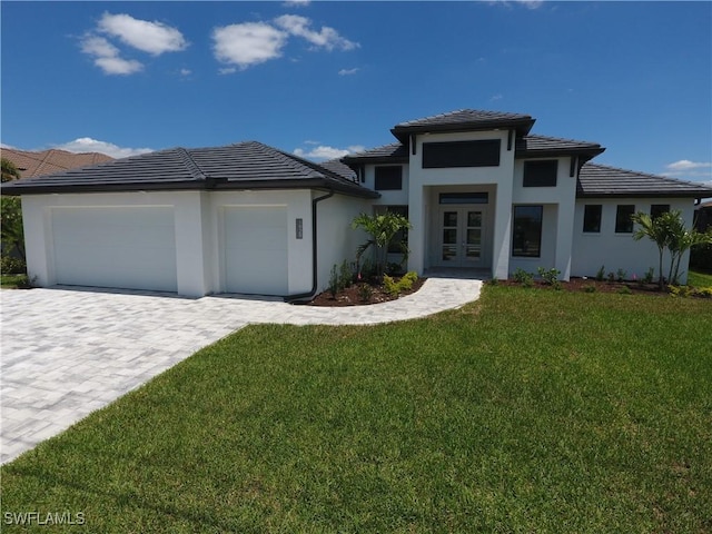 prairie-style house featuring a front lawn, decorative driveway, french doors, an attached garage, and a tiled roof