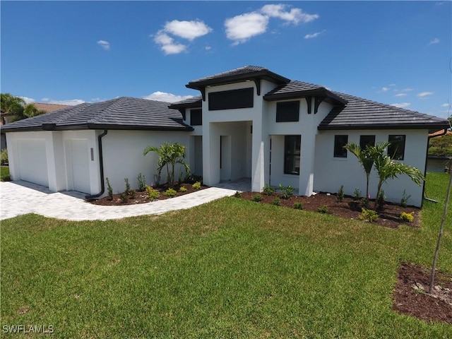 prairie-style house with a tile roof, a front yard, stucco siding, decorative driveway, and a garage