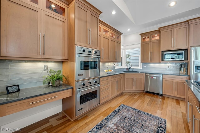 kitchen featuring light wood-style floors, decorative backsplash, stainless steel appliances, and a sink