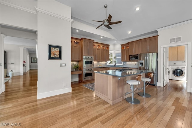 kitchen with washing machine and clothes dryer, visible vents, appliances with stainless steel finishes, ornamental molding, and a kitchen breakfast bar