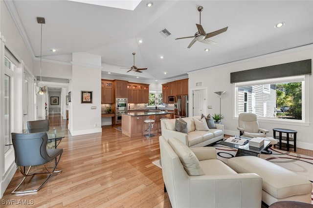 living area with ceiling fan, recessed lighting, ornamental molding, light wood finished floors, and lofted ceiling with skylight