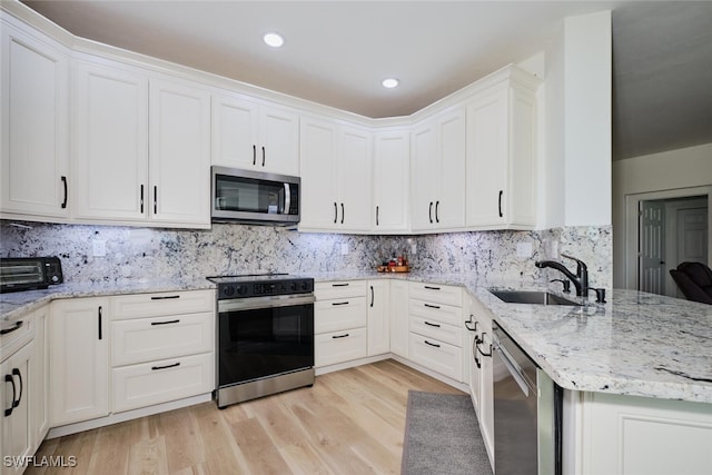 kitchen featuring appliances with stainless steel finishes, light wood-style floors, a sink, and a peninsula