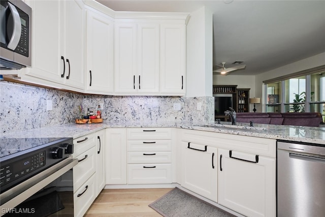 kitchen featuring stainless steel appliances, a sink, white cabinets, light wood-type flooring, and light stone countertops