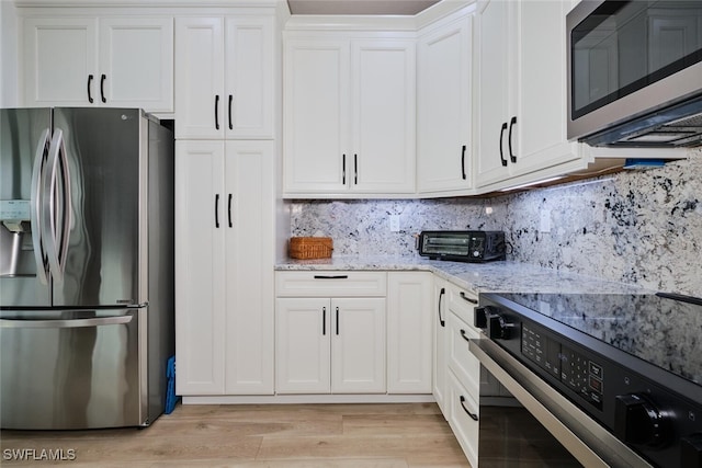 kitchen featuring light stone counters, stainless steel appliances, light wood-style flooring, decorative backsplash, and white cabinetry