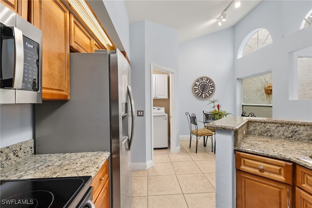 kitchen with brown cabinets, light tile patterned floors, stainless steel microwave, light stone countertops, and washer / dryer